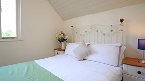 Quarto com cama, mesa de cabeceira com um vaso de flores, luminária e janela.