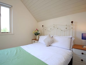 Un dormitorio con cama, una mesita de noche con un florero, una lámpara y una ventana.