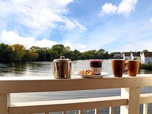 Vista fluvial amb un pont de fusta, un contenidor metàl·lic, un plat amb croissants i melmelada, i dues tasses.