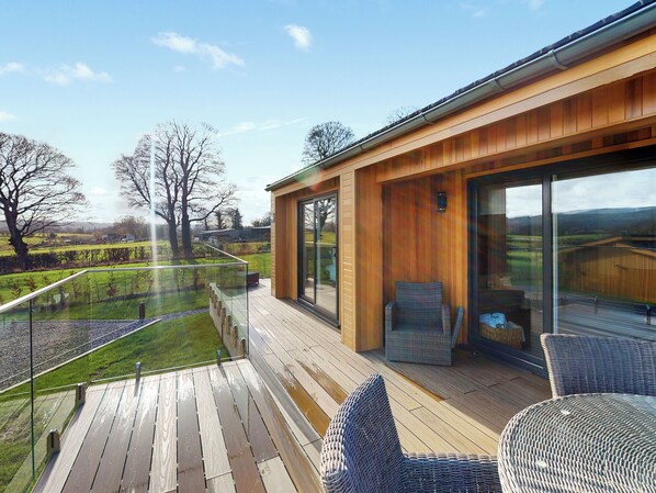 Une terrasse extérieure moderne, dotée de rampes en verre, de meubles en osier et offrant une vue sur la campagne.