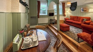 A dining area with a wooden table, chairs, and a tray with teapots and cups. There is a red sofa and a patterned rug in the living area. - Saddle Room - UK51017 (Louth)