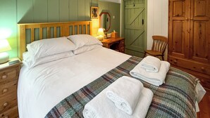 A neatly made bed with pillows and a folded towel, a bedside lamp, a wooden nightstand, a green door, and a wooden wardrobe. - Saddle Room - UK51017 (Louth)