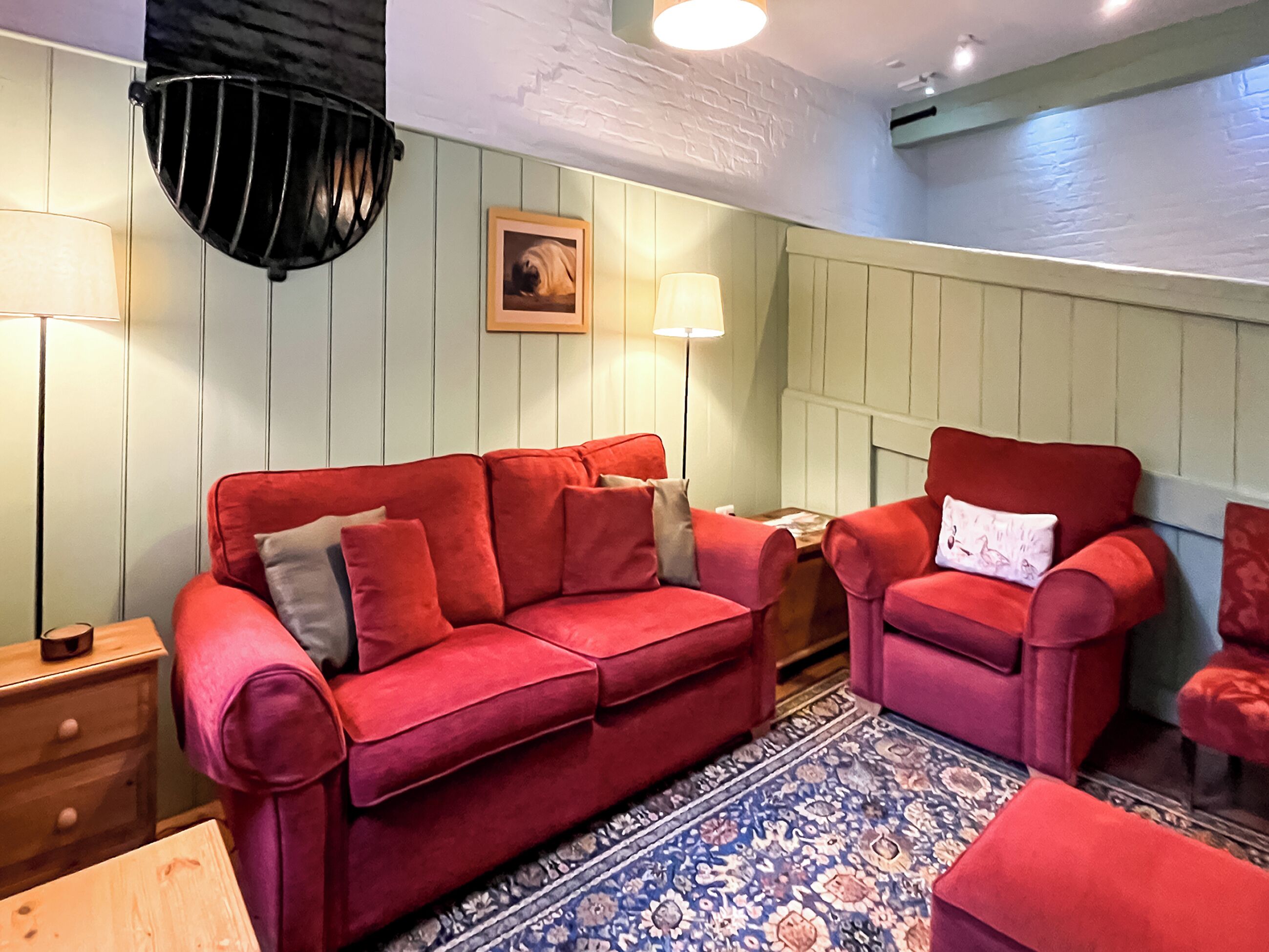 Una habitación acogedora con un sofá rojo, un sillón a juego, una alfombra estampada y una lámpara de pared.