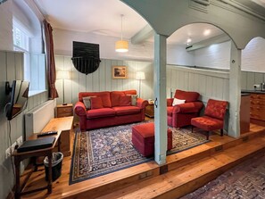 A cozy living room with a red sofa, a matching armchair, and a wooden coffee table. There is a patterned rug on the floor, and a lamp hangs from the ceiling. - Saddle Room - UK51017 (Louth)