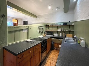 Una cocina compacta con gabinetes verdes, encimera negra, microondas y un lavamanos.