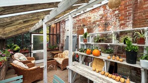 A covered patio with wicker furniture, a wooden table, and a shelf with potted plants and pumpkins. - Saddle Room - UK51017 (Louth)