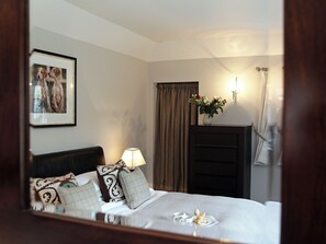 A hotel room with a bed, a framed picture on the wall, a bedside lamp, a vase with flowers, and a mirror reflecting the room. - 1 bedroom accommodation in Near Stow-on-the-Wold (Near Stow-on-the-Wold)