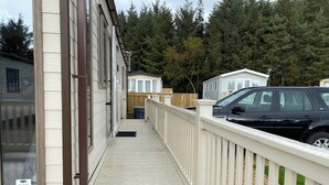 Eine Holzterrasse mit weißer Reling, die zu einem Gebäude mit großen Fenstern und einer Tür führt.