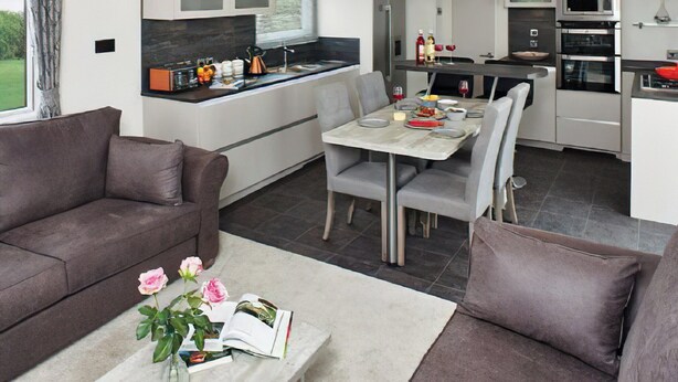 Eine moderne Küche mit weißen Schränken, ein Essbereich mit grauen Stühlen und ein graues Sofa.