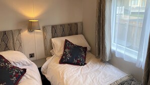 Ein Hotelzimmer mit zwei Betten, einer Wandlampe und einem Fenster mit durchsichtigen Vorhängen.