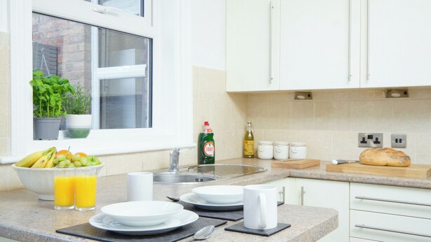 Cocina con armarios blancos, una ventana con plantas, un lavabo y una encimera con un pan.