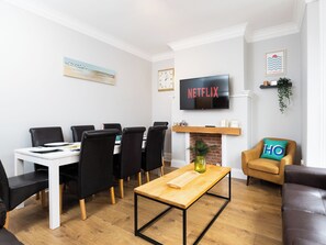 A modern living room with a white fireplace, a dining table with chairs, a TV mounted on the wall, and a cozy seating area with a sofa and a chair. - Ashville Lodge - UK37119 (Scarborough)