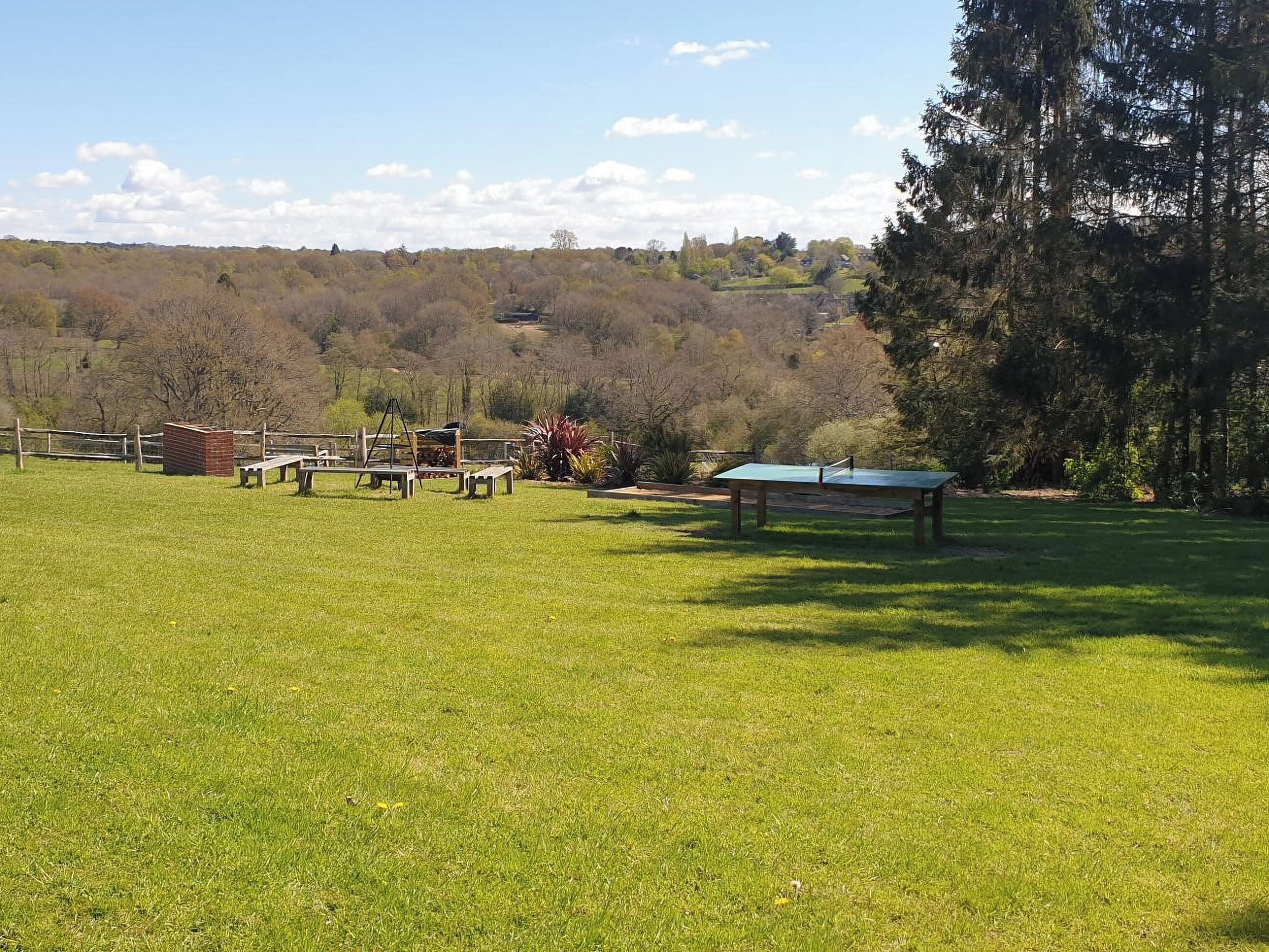 Un'area verde all'aperto con tavolo da ping pong, tavoli da picnic e una struttura in mattoni.