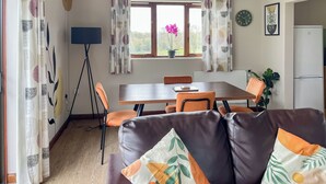 Ein gemütliches Wohnzimmer mit einem braunen Ledersofa, einem Esstisch mit Stühlen, einem Stativ und einem Blumentopf.