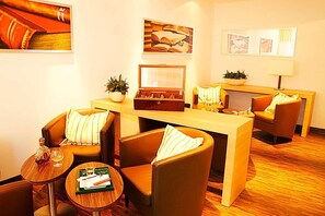A modern hotel room with a wooden desk, leather armchairs, a small round table, and a bookshelf. - H Hotel Zurich (Zürich)
