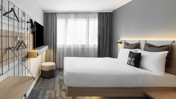 A modern hotel room with a bed, a TV, a wardrobe, and a window with curtains. - H Hotel Zurich (Zürich)