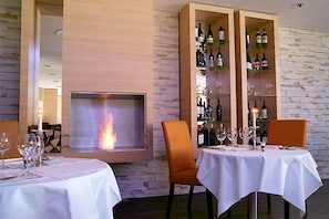 Un comedor con chimenea, dos mesas dispuestas para comer y una vitrina para vinos.