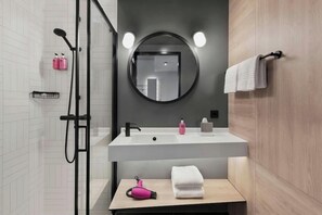 A modern bathroom with a glass shower enclosure, a white sink with a round mirror, and a wooden vanity with a towel rack. - H Hotel Zurich (Zürich)