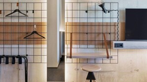A modern room with a grid-patterned wall, a wooden bench, a hanging light fixture, and a TV mounted on the wall. - H Hotel Zurich (Zürich)
