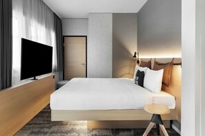 A modern hotel room with a large bed, a flat-screen TV, a bedside table, and a lamp. - H Hotel Zurich (Zürich)