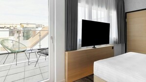 A hotel room with a balcony, a bed, a TV, and a desk. - H Hotel Zurich (Zürich)