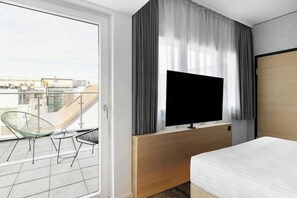 A hotel room with a balcony, a bed, a TV, and a desk. - H Hotel Zurich (Zürich)