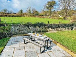 A stone patio with a picnic table set for four, surrounded by a stone wall and a grassy field. - 3 bedroom accommodation in Beaumaris (Beaumaris)