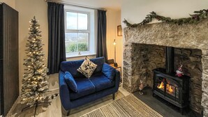 A cozy living room with a blue sofa, a Christmas tree, a stone fireplace, and a window with curtains. - 3 bedroom accommodation in Beaumaris (Beaumaris)