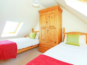 A bedroom with two beds, a wooden wardrobe, and a skylight.