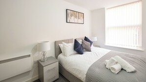 Une chambre à coucher moderne, avec un lit, des tables de chevet et une fenêtre équipée de stores.
