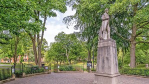 Un parc avec une statue, des allées pavées et des arbres.