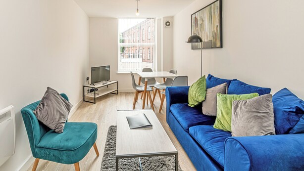 Una sala de estar moderna con un sofá azul, un sillón color turquesa y un televisor pequeño sobre un mueble.
