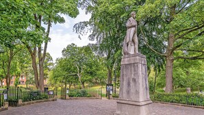 Un parque con una estatua, senderos pavimentados y árboles.