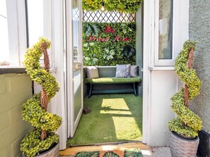 A doorway leading to a green lawn area with a bench and a wall covered in foliage.