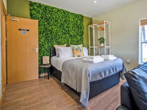A modern bedroom with a green wall, a bed with white bedding, a wooden door, and a small bedside table.