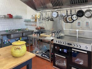 A kitchen with stainless steel appliances, a clock, hanging pots, and a yellow pot on a table.