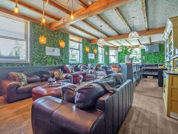 A cozy lounge area with leather sofas, a bar, and green walls.