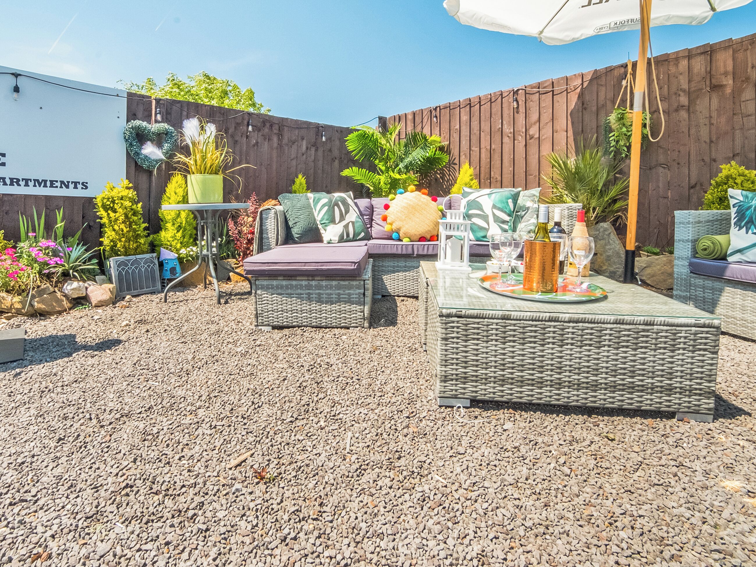 A patio area with outdoor furniture, a table with drinks, and a wooden fence.