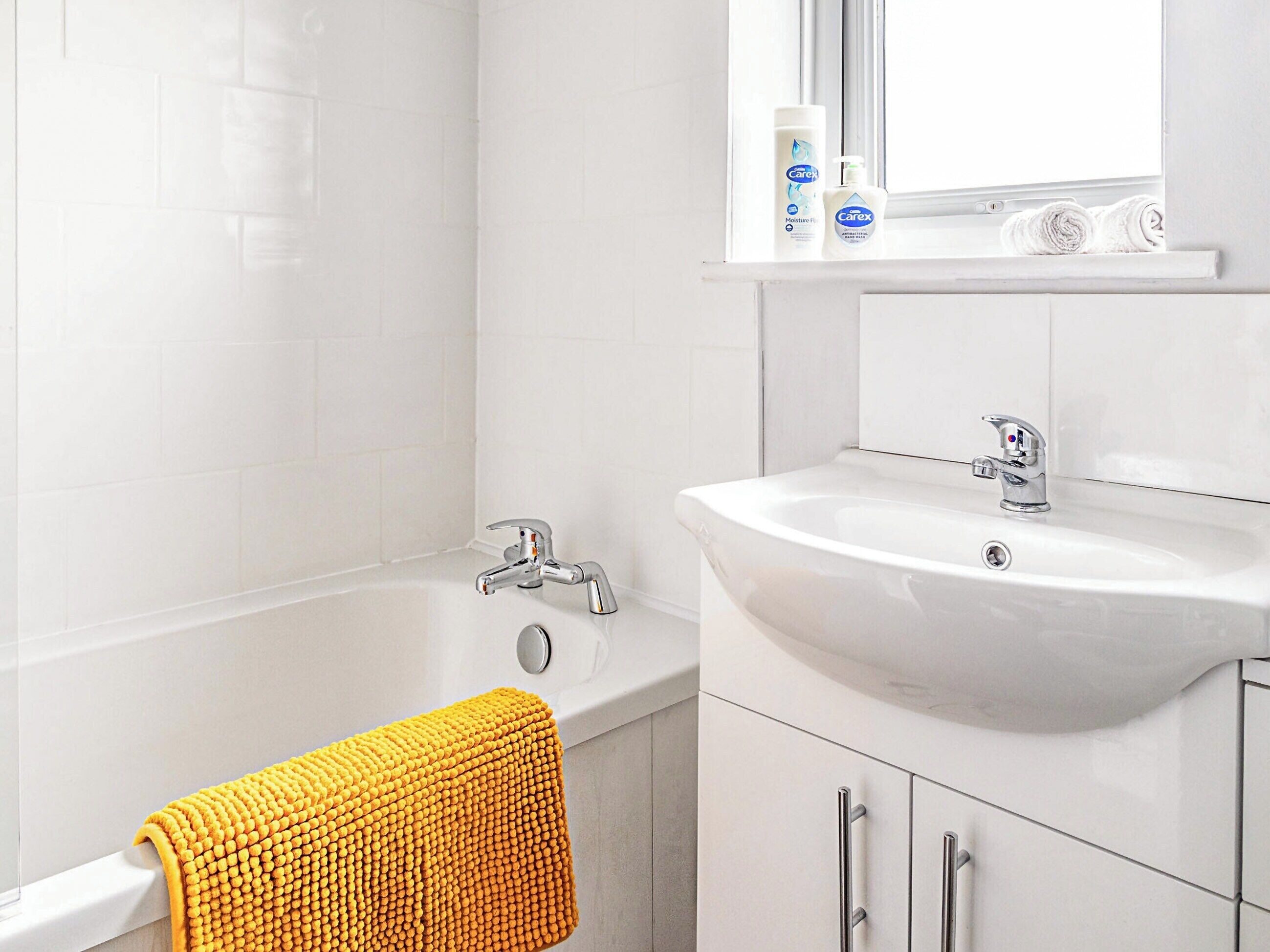 A bathroom with a white bathtub, a sink, and a window above the mirror.