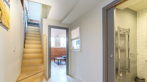 Un interior moderno con una escalera de madera, un pasillo que lleva a un comedor y un baño con perchero.