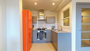 Una cocina compacta con un refrigerador naranja brillante, un horno empotrado y un lavamanos.