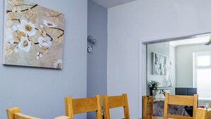 Een eetgedeelte met een houten tafel en stoelen, een kunstwerk aan de muur, en een spiegel die de kamer weerspiegelt.