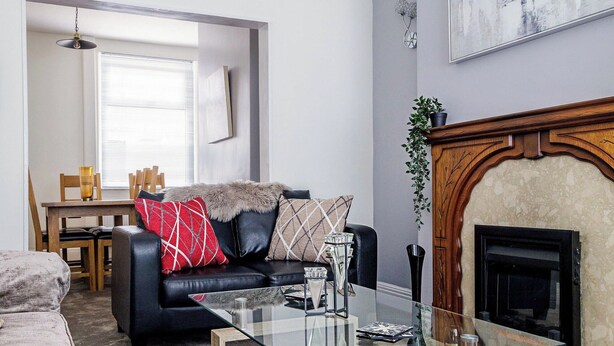 Een woonkamer met een glazen salontafel, een open haard, een bank met decoratieve kussens, en een eethoek op de achtergrond.