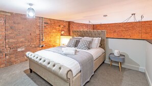 Ein Schlafzimmer mit Backsteinwand, einem bettgestellten Bett, einem Nachttisch mit Lampe und einem kleinen dekorativen Gegenstand.