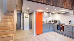 Eine moderne Küche mit grauen Schränken, einer Holztreppe und einem leuchtend orangefarbenen Kühlschrank.