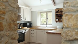 A kitchen with white cabinets, a microwave, an oven, a window, and a stone wall.
