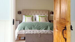 A bedroom with a tufted headboard, two bedside lamps, a bed with a green and white bedspread, and a wooden door.