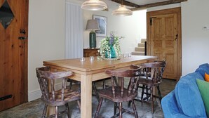 A dining area with a wooden table, six chairs, two pendant lights, a vase with flowers, and a lamp on a side table.