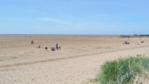 A wide sandy beach with a few people and beach chairs.