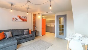 A modern living room with a grey sectional sofa, a dining table with chairs, and a kitchen in the background.